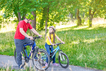 Plakat Father and her daughter cycling in the summer park together. Empty space for text