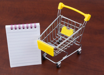 Yellow shopping cart and blank notepad page, buy and sale concept