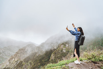 Happy woman tourist taking selfie using smartphone on top of a mountain