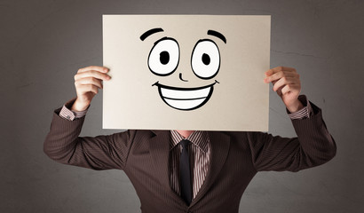 Young student holding a paper with laughing emoticon in front of his face