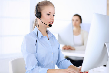 Call center office. Beautiful blonde woman using computer and headset for consulting clients...