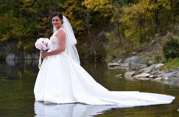 Fototapeta na wymiar Bride holding a bouquet of different flowers. Beautiful bride in white dress walking in the water, natural background. Czech republic, Europe.