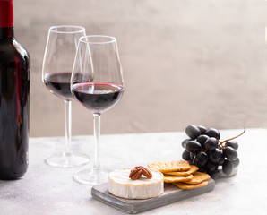 Two Red wine glasses and charcuterie board with different snacks for wine. French Cheese, grapes and crackers.
