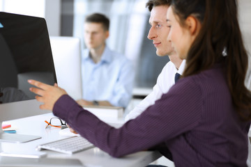 Business woman and man discussing questions while using computer at workplace in modern office. Teamwork, meeting and brainstorming concept