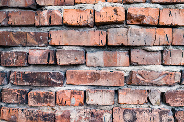 The background is made of red bricks with a wavy relief, cracks, holes and ditches. Building material for decoration and decor in the style of a loft.