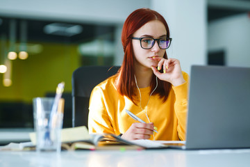 Young girl works at a computer in the office. Beautiful freelancer working from a laptop computer....
