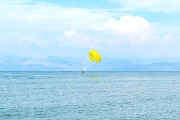 Yellow parachute in the blue sky over the sea on the island of Corfu, Greece. Parasailing extreme sports on the beach.