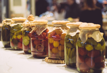 Pickled cucumbers and tomatoes in glass jars on the table. Pickles from vegetables. Vegetarian food