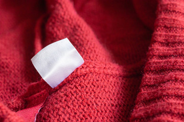 Blank white laundry care clothing label on red knitted texture background