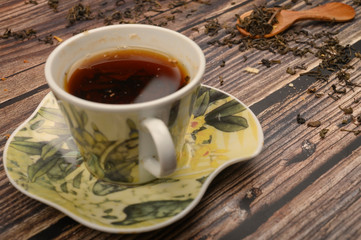 Cup of black tea, tea leaves in a wooden spoon on a wooden background. Close up.
