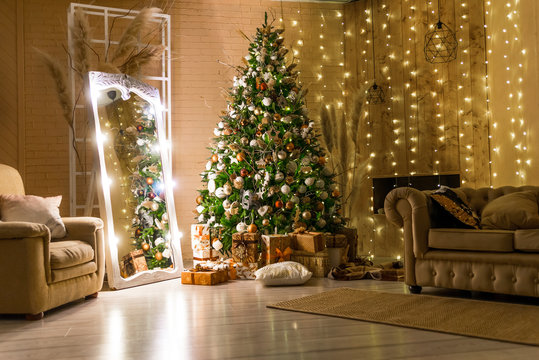 decorated for Christmas house. big beautiful spruce. beautiful Christmas room with lights and garlands. Christmas tree decoration, fireplace and sofas in a cozy room. Christmas Studio with wooden wall