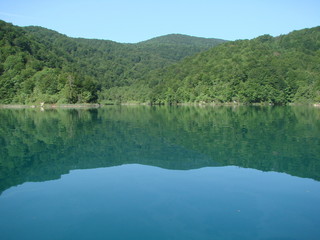 View from the deck of the ship on the quiet azure surface of the lake surrounded by mountain forest that densely covers its shores.
