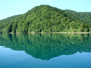 View from the deck of the ship on the quiet azure surface of the lake surrounded by mountain forest that densely covers its shores.