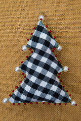 Handmade checkered textile cotton fabric naive retro style Christmas tree ornament decorated with beads on burlap background