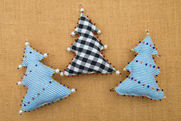 Handmade striped and checkered textile cotton fabric naive retro style Christmas tree ornament decorated with beads on burlap background