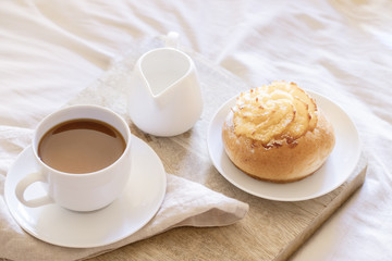 Morning Breakfast In Bed ,  cup of coffee and sweet bun on wooden tray on beige white sheets. Good morning scenery background. Scandinavian style.