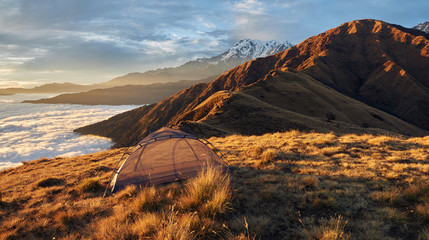 A small tent without an awning, on the edge of a high hill, against the backdrop of the mountains, along the route to the eastern base camp of Mardi Himal. Magical sea view of clouds at sunset