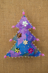 Handmade floral purple  blue textile cotton fabric naive retro style Christmas tree ornament decorated with beads on burlap background