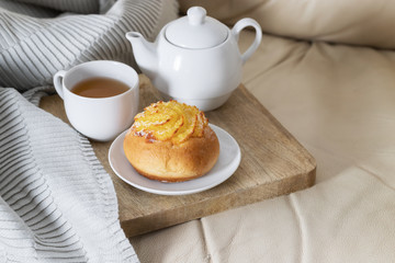 Grey blanket, wooden try with  tea and sweet bun on white sofa. Hygge Relax and stay at home concept.