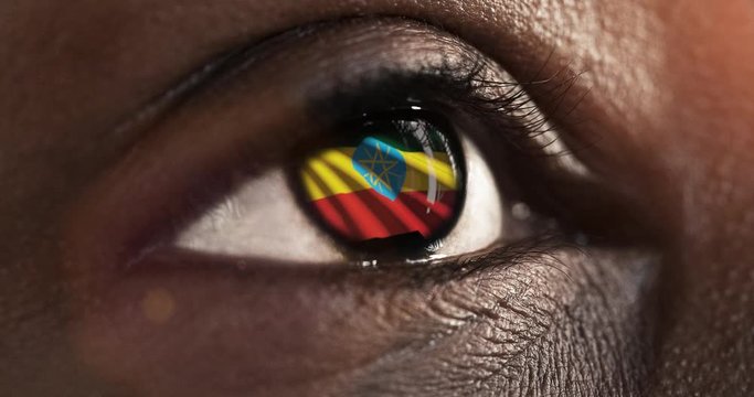 Woman black eye in close up with the flag of Ethiopia in iris with wind motion. video concept