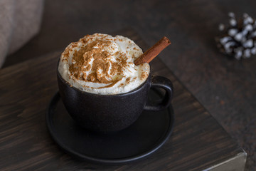 Cup of coffee with milk foam cream and cinnamon on wooden background. Hot beverage for cold winter days concept.