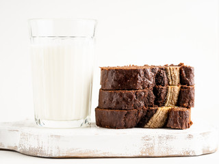 Gorgeous tasty chocolate banana cake (banana bread) sliced and decorated with banana split on white wooden cutting board with a glass of milk, white background