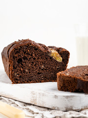 Gorgeous tasty chocolate banana cake (banana bread) sliced and decorated with banana split on white wooden cutting board with a glass of milk, white background