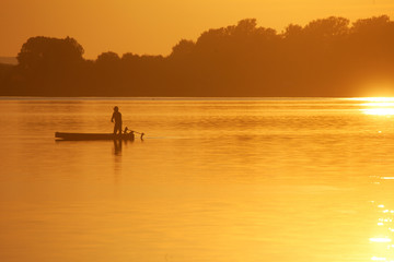 Naklejka na ściany i meble Silhouette of the fisherman on the boat during sunset on the Soderica Lake, Croatia