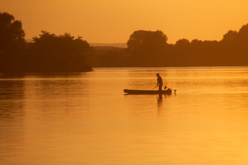 Naklejka na ściany i meble Silhouette of the fisherman on the boat during sunset on the Soderica Lake, Croatia