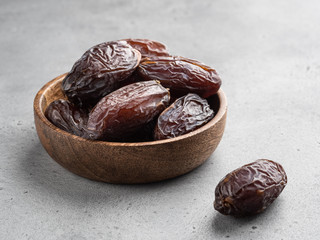 Healthy natural raw dessert, dried medjool dates in wooden plate, gray background, closeup view.
