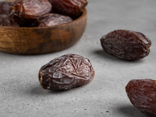 Healthy natural raw dessert, dried medjool dates in wooden plate, gray background, closeup view.