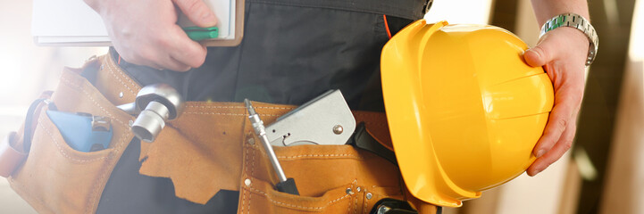 unknown handyman with hands on waist and tool belt with construction tools against grey background....