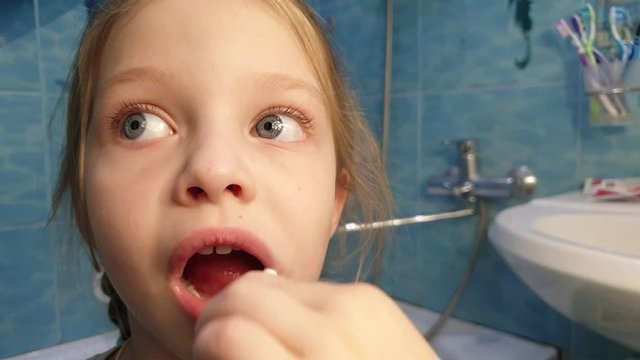 Little girl f brushing her teeth with a toothbrush in bathroom in the morning.