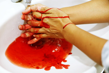 Close up washing the blood out of the hands in the bathroom.