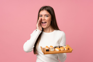 Young girl with sushi over isolated pink background shouting with mouth wide open © luismolinero