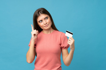 Young woman over isolated blue background holding a credit card