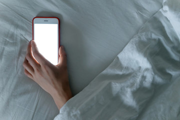 Smartphone laying in hand of sleeping female under blanket. Phone dependence and overuse. Internet addiction concept. Horizontal shot. Focused on phone.
