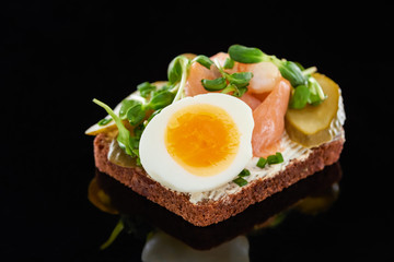 close up of boiled egg near salmon on danish smorrebrod sandwich on black
