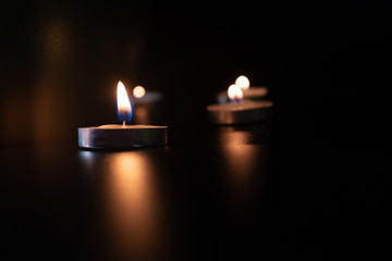 GROUP OF SMALL ROUND CANDLES LIGHTED IN VERY SOFT ENVIRONMENT WITH BLACK BACKGROUND