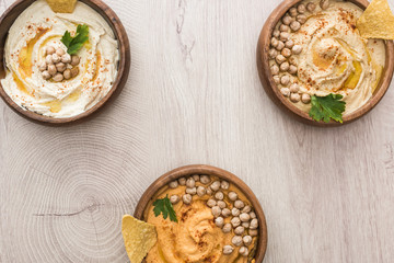 top view of delicious hummus with chickpeas and nachos in bowls on beige wooden table
