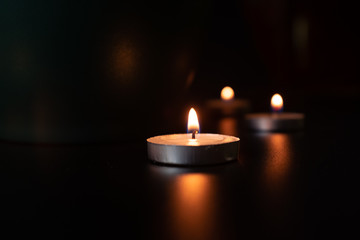 GROUP OF SMALL ROUND CANDLES LIGHTED IN VERY SOFT ENVIRONMENT WITH BLACK BACKGROUND