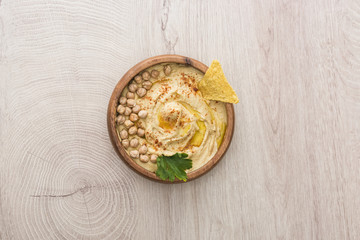 Fototapeta na wymiar top view of delicious hummus with chickpeas and nacho in bowl on beige wooden table