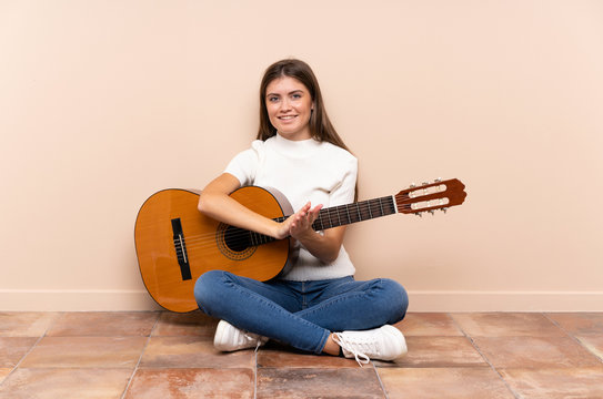 Young woman with guitar sitting on the floor applauding