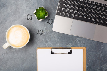 Office Flat lay gray desk with silver laptop computer, coffee, and blank paper list and stationery. Mockup copy space.