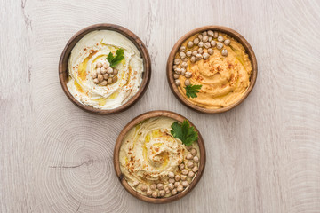 top view of delicious hummus with chickpeas in bowls on beige wooden table