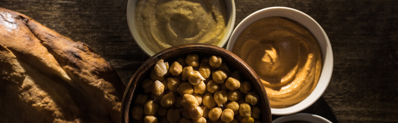 top view of delicious assorted hummus, chickpeas and fresh baked pita on wooden rustic table, panoramic shot