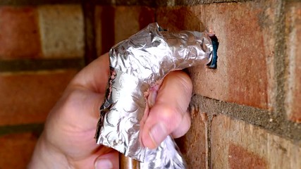 Closeup of a man’s hands wrapping reflective foil spiral lagging / insulation around exposed bare copper water pipe and brass fitting, to protect against freezing in winter.