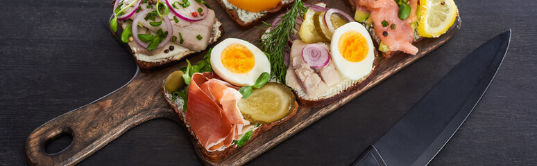 panoramic shot of wooden cutting board with danish smorrebrod sandwiches near knife on grey surface
