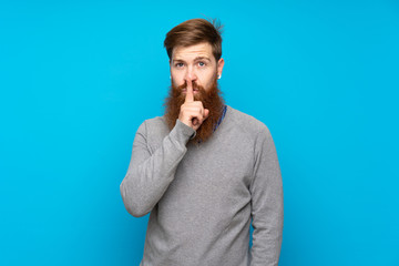 Redhead man with long beard over isolated blue background showing a sign of silence gesture putting...