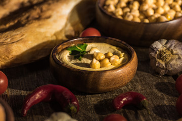 selective focus of delicious hummus, chickpeas, pita, vegetables and spices on wooden rustic table